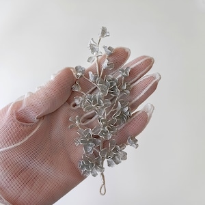 Puede incluir: Peine de pelo floral plateado con detalles delicados e intrincados. El peine está hecho de metal y presenta un grupo de pequeñas flores plateadas.