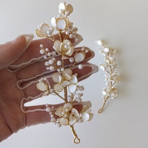 Puede incluir: Dos piezas de pelo florales blancas y doradas con cuentas de perlas. Las piezas de pelo están hechas de alambre y tienen un diseño delicado y femenino.