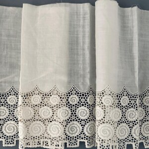 Puede incluir: Tela blanca con un borde de encaje decorativo. El encaje presenta un patr&oacute;n repetitivo de dise&ntilde;os en espiral y bordes festoneados. La tela parece ligera y semitransparente, adecuada para cortinas u otros proyectos de decoraci&oacute;n del hogar.