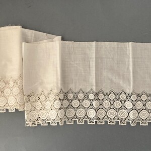 Puede incluir: Dos piezas de tela blanca dobladas con un borde decorativo calado. El borde presenta un patr&oacute;n repetitivo de espirales y c&iacute;rculos, creando un borde delicado y calado. La tela parece ligera, posiblemente lino o algod&oacute;n.