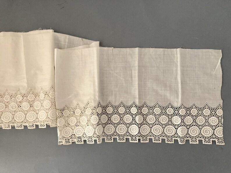 Puede incluir: Dos piezas de tela blanca dobladas con un borde decorativo calado. El borde presenta un patr&oacute;n repetitivo de espirales y c&iacute;rculos, creando un borde delicado y calado. La tela parece ligera, posiblemente lino o algod&oacute;n.