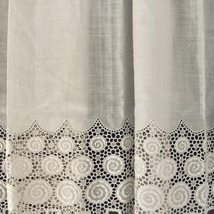 Puede incluir: Cortinas blancas transparentes con un borde de encaje festoneado decorativo. El encaje presenta un patr&oacute;n repetitivo de dise&ntilde;os en espiral. Las cortinas est&aacute;n hechas de una tela ligera, lo que permite que la luz se filtre.