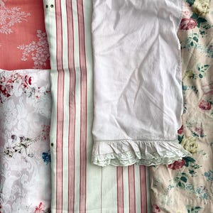 Puede incluir: Surtido de piezas de tela vintage en varios patrones y colores. Incluye un estampado floral coral, una tela a rayas blancas y rojas, una prenda blanca con ribete de encaje y una tela estampada floral con flores rosas y azules.