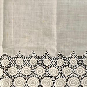 Puede incluir: Tela blanca con un borde calado decorativo. El borde presenta un patr&oacute;n repetitivo de dise&ntilde;os en espiral dentro de marcos circulares, conectados por un delicado enrejado geom&eacute;trico. La tela parece ligera, posiblemente lino o algod&oacute;n, con alguna decoloraci&oacute;n menor.