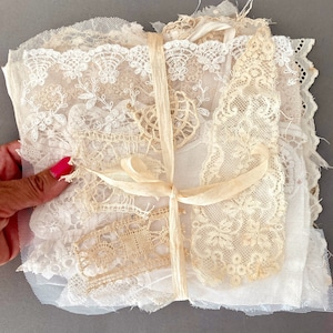 Può includere: Un fascio di assortiti pezzi di pizzo vintage nei toni crema e avorio, legato con un nastro color crema. Il pizzo presenta vari motivi, tra cui disegni floreali e geometrici, e diverse trame. Il fascio è legato con un nastro color crema.