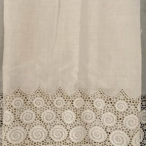 Puede incluir: Tela blanca con un borde de encaje calado decorativo. El encaje presenta un patr&oacute;n repetitivo de dise&ntilde;os en espiral y un borde festoneado. La tela parece ser un material ligero, posiblemente lino o algod&oacute;n.