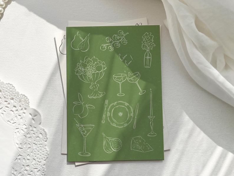 May include: A green card with white line drawings of various objects, including fruit, glasses, a plate, and a candle. The text "Cheers!" is written on the card.
