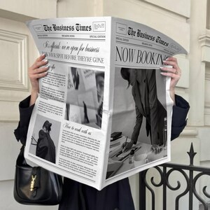 May include: A person holding open a newspaper titled "The Business Times." The newspaper's headline reads "NOW BOOKING" and includes the text "It's official, we're open for business. BOOK YOUR SPOT BEFORE THEY'RE GONE."