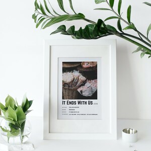 Może przedstawiać: Biała oprawa z czarno-białym plakatem dla książki "It Ends With Us" Colleen Hoover. Plakat zawiera tytuł książki, autora, gatunek, serię i aktor&oacute;w grających gł&oacute;wne role. Plakat przedstawia zdjęcie koszyka z r&oacute;żowymi kwiatami.