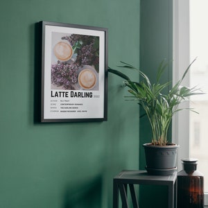 Może przedstawiać: Czarny plakat w ramie z białym tłem i minimalistycznym wzorem. Plakat przedstawia zdjęcie dw&oacute;ch filiżanek kawy z latte art i fioletowymi kwiatami. Tekst na plakacie brzmi "Latte Darling 2022" i zawiera informacje o autorze, gatunku, serii i gł&oacute;wnych aktorach.