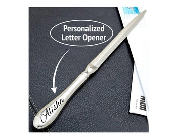 May include: Silver letter opener with a personalized inscription that reads "Alisha". The opener is on a black leather surface with a white envelope in the background. The text "Personalized Letter Opener" is in a white oval above the opener.