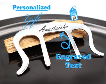 Puede incluir: Porta incienso de metal plateado con un nombre grabado personalizado "Anastaisha". El porta incienso está diseñado para sostener un palo de incienso y tiene una forma curva. El texto "Texto grabado" también es visible en el porta incienso.
