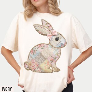 May include: A white t-shirt with a patchwork bunny design. The bunny is made of different fabrics in shades of pink, blue, and yellow. The bunny has a pink bow on its head.