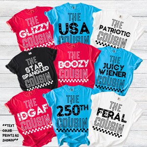 May include: A collection of colorful t-shirts with various phrases, including "The Glizzy Cousin," "The USA Cousin," and "The Patriotic Cousin." The shirts are red, blue, black, and white, with bold, white text and a checkered border.