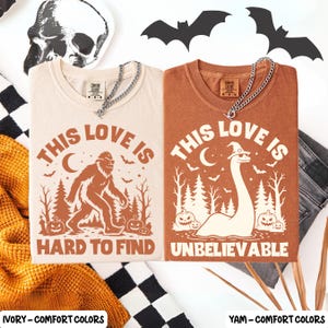 May include: Two short-sleeve crew neck t-shirts in ivory and yam colors. The ivory shirt features a brown graphic of Bigfoot, pumpkins, trees, and the text THIS LOVE IS HARD TO FIND. The yam shirt shows a Loch Ness monster, pumpkins, and THIS LOVE IS UNBELIEVABLE.