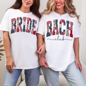 May include: Two white t-shirts with patriotic designs. One shirt says "BRIDE" in red, white, and blue patterned letters. The other says "BACH club" in similar colors. Both shirts have short sleeves and are worn with blue jeans.