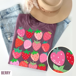May include: A purple t-shirt with a strawberry graphic. The shirt features multiple strawberries in shades of pink and red with green leaves. The text "Hail Satan" is printed on each strawberry. The word "BERRY" is printed at the bottom left.