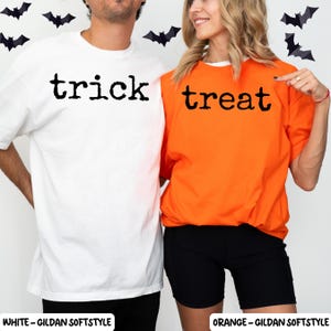 May include: A white t-shirt with the black text trick and an orange t-shirt with the black text treat. Both shirts feature short sleeves and a crew neckline. The shirts are displayed against a white background with black bat silhouettes.