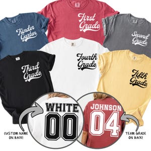 May include: Various coloured t-shirts with grade level text, including "Kindergarten", "First Grade", "Second Grade", "Third Grade", "Fourth Grade", and "Fifth Grade". Two shirts show custom names and team grades on the back.