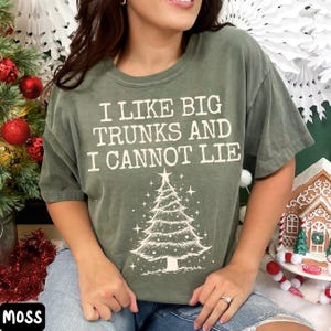 Peut inclure: T-shirt vert mousse avec l'inscription "I LIKE BIG TRUNKS AND I CANNOT LIE" surmontant un sapin de No&euml;l. Le t-shirt est de coupe d&eacute;contract&eacute;e, id&eacute;al pour la saison des f&ecirc;tes.