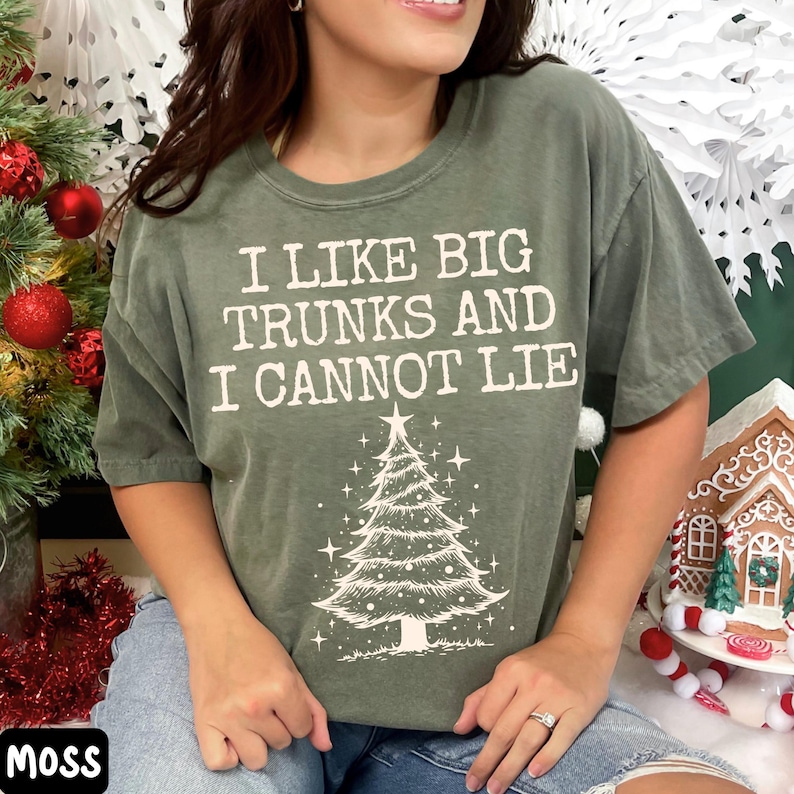 Peut inclure: T-shirt vert mousse avec l'inscription "I LIKE BIG TRUNKS AND I CANNOT LIE" surmontant un sapin de No&euml;l. Le t-shirt est de coupe d&eacute;contract&eacute;e, id&eacute;al pour la saison des f&ecirc;tes.