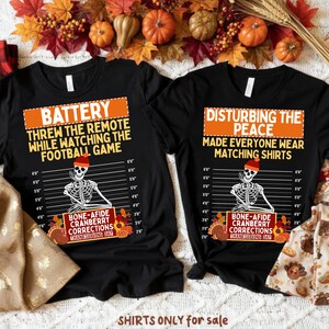 Może przedstawiać: Dwie czarne koszulki z zabawnymi tekstami i grafikami o tematyce Święta Dziękczynienia. Na jednej koszulce widnieje napis "BATTERY THREW THE REMOTE WHILE WATCHING THE FOOTBALL GAME". Na drugiej napis "DISTURBING THE PEACE MADE EVERYONE WEAR MATCHING SHIRTS."