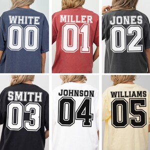 May include: Six t-shirts in various colours, including navy, red, charcoal, black, white, and yellow, are shown. Each shirt has a name and number printed on the back in a collegiate style font, with the numbers outlined in black.