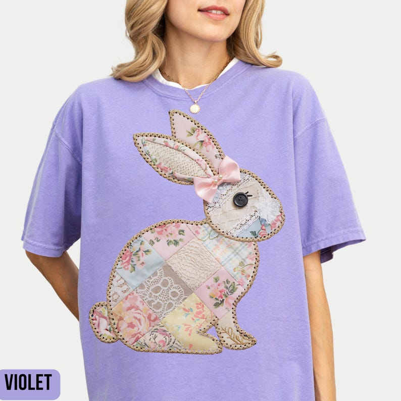 May include: A purple t-shirt with a patchwork bunny applique. The bunny is made of different fabrics in shades of pink, white, and brown. The bunny has a pink bow on its head.