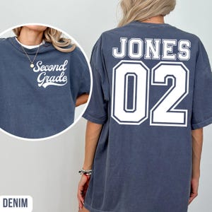 May include: Denim-coloured t-shirt with the text "Second Grade" on the front and "JONES 02" on the back in white lettering. The shirt has a crew neck and short sleeves. The shirt is a relaxed fit.