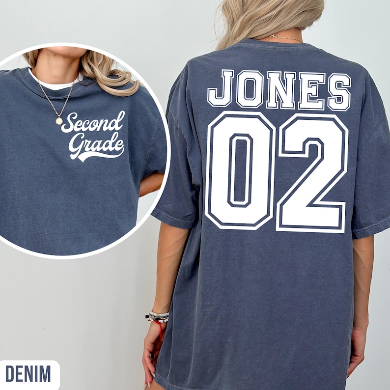 May include: Denim-coloured t-shirt with the text "Second Grade" on the front and "JONES 02" on the back in white lettering. The shirt has a crew neck and short sleeves. The shirt is a relaxed fit.