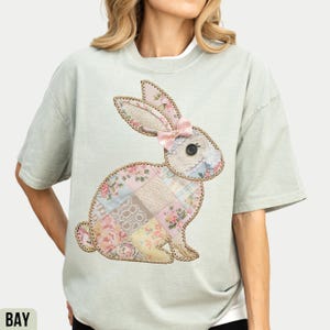 May include: A light green t-shirt with a patchwork bunny applique. The bunny is made of various floral and lace fabrics and has a pink bow.