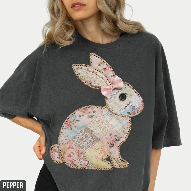 May include: A dark gray t-shirt with a patchwork bunny applique. The bunny is made of various fabrics in shades of pink, white, and blue, with floral patterns. The bunny has a pink bow on its head.