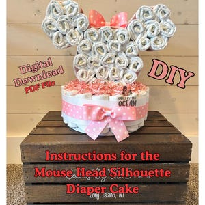 May include: A DIY diaper cake in the shape of a mouse head, with rolled diapers forming the ears. The cake is decorated with pink polka dot ribbon and a bow. Text on the image reads "Digital Download PDF File" and "Instructions for the Mouse Head Silhouette Diaper Cake."