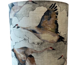 May include: A cylindrical lampshade with a beige linen fabric featuring a watercolor-style print of flying cranes in shades of brown, gray, and red.