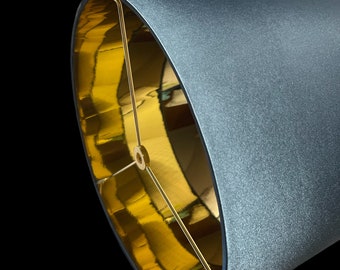 May include: A gray lampshade with a gold interior. The lampshade is made of fabric and has a textured surface.