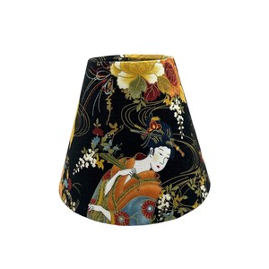 May include: A black lampshade with a floral pattern featuring a geisha in a kimono. The pattern includes gold accents and various flowers.