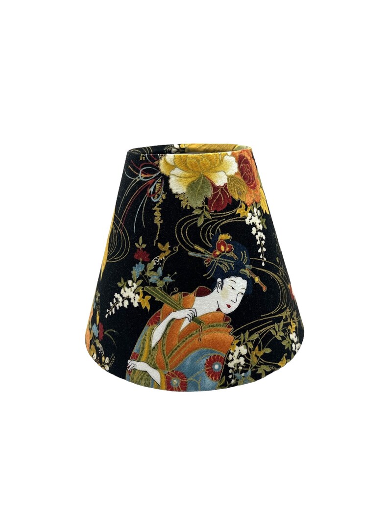 May include: A black lampshade with a floral pattern featuring a geisha in a kimono. The pattern includes gold accents and various flowers.
