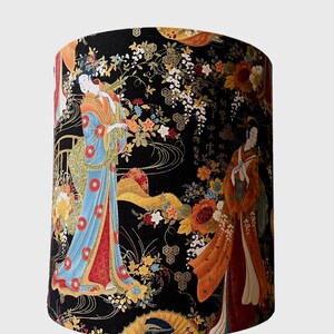 K&ouml;nnte beinhalten: Ein schwarzer Lampenschirm mit einem goldenen Dreibeinst&auml;nder zeigt einen Blumendruck mit zwei Frauen in traditioneller japanischer Kleidung. Der Druck enth&auml;lt goldene Akzente und einen schwarzen Hintergrund.