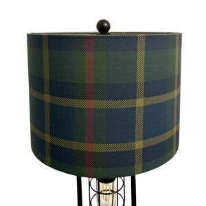 May include: A black floor lamp with a green, blue, and yellow plaid lampshade. The lamp has a cage-like base with a visible light bulb.