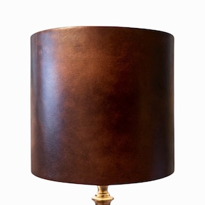 May include: A brown cylindrical lampshade with a textured surface sits atop a gold-colored lamp base. The lampshade has a warm, earthy tone, and the lamp base has a classic, elegant design. This lamp is suitable for home decor.