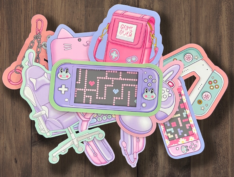 May include: A collection of colorful stickers with a gaming theme. Designs include a pink handheld console with "GAME OVER" text, a purple gaming chair, and a handheld console with a maze game. Other stickers feature a cat face, a bunny controller, and a pink purse.