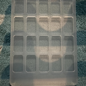 May include: A rectangular, translucent silicone mold featuring a grid of twenty recessed, rounded rectangular cavities. The base of the mold includes embossed text reading WKS MARKERS 3.5mm 1.75 x 1.25. The mold has a smooth, matte finish and a uniform thickness.