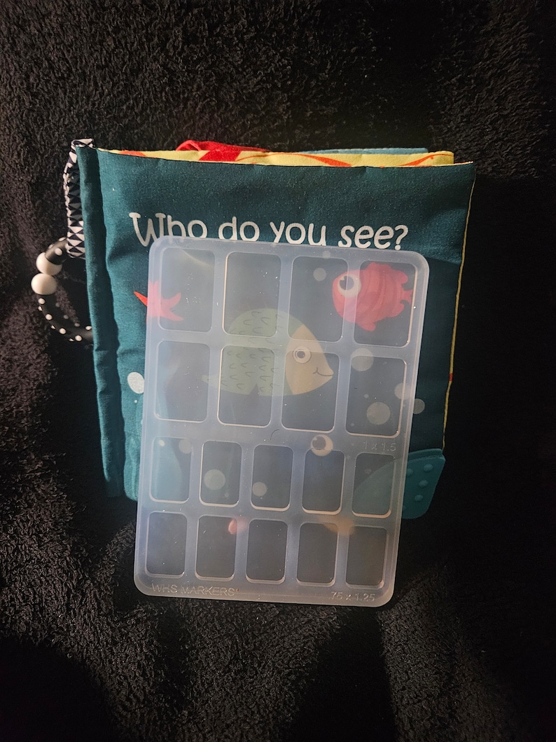 May include: A clear plastic storage box with 15 compartments. The box has the words "WHS MARKERS" and "1x1.5" printed on the bottom.