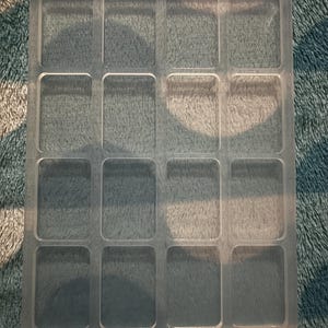 May include: A rectangular, translucent silicone mould featuring sixteen individual, rounded-corner rectangular cavities arranged in a four-by-four grid. The bottom edge displays the embossed text WHS MARKERS 3.5mm and 1.0 / 1.5.