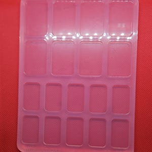 May include: A clear plastic mold with 16 rectangular compartments. The mold is designed for making small crafts or resin projects.