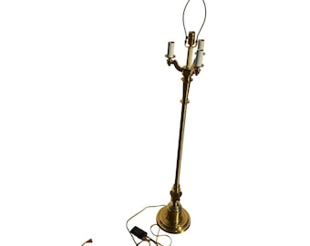 May include: A tall, polished brass floor lamp featuring a slender central column, a round base, and a multi-arm top assembly with three light bulb sockets and a harp attachment. A long electrical cord with a black switch extends from the base.
