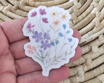 May include: A watercolor sticker featuring a bouquet of flowers in shades of pink, purple, blue, and yellow. The flowers are arranged in a loose, natural style, and the sticker has a white background.