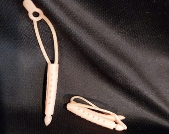 May include: Two light pink plastic cord locks on a black background. One cord lock is open, with a loop at the top and a series of holes along the body. The other cord lock is closed, with a curved top and a series of holes.