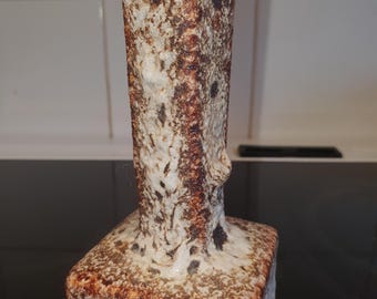 Puede incluir: Un jarrón de cerámica texturizada, de forma rectangular con base cuadrada y cuerpo alto y estrecho. El jarrón tiene un aspecto moteado con tonos marrones, crema y manchas oscuras. Diseño rústico y artístico.