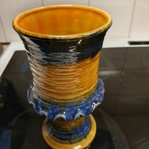 May include: A ceramic goblet with a blue and orange glaze. The goblet has a fluted rim and a wide base.